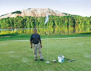 Stone Mountain GC employee Gibbs Valcin stands next to the first 8-inch cup cut at the course, immediately after aerification.