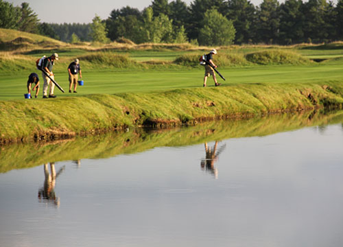 The only water feature on the course (other than Lake Michigan), the crew works to tidy up No. 5 fairway with their reflections bouncing off the water.