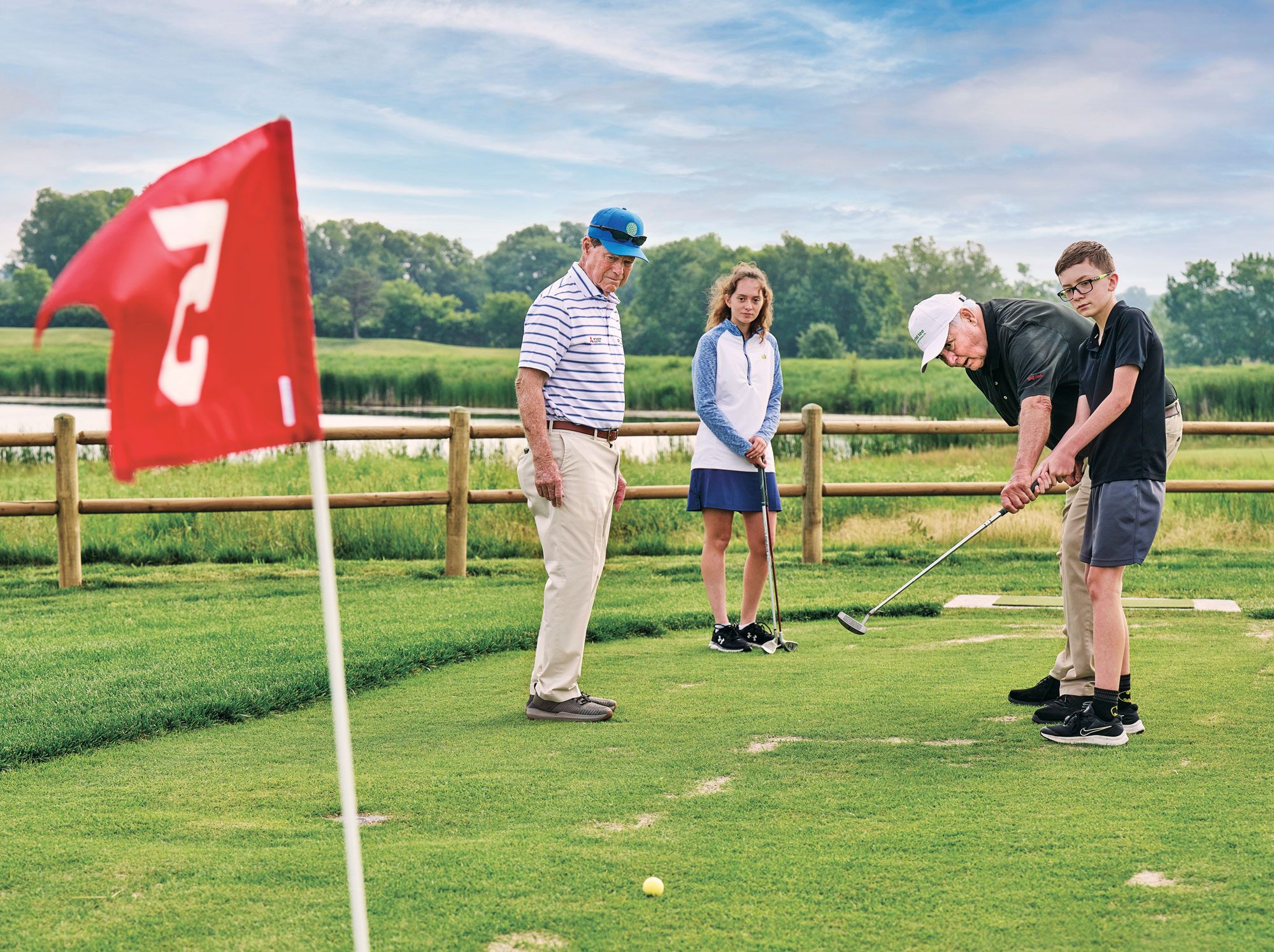 Tom Watson and Evey Jones (age 16) watch as Jeff Burey guides Boyd Jones (age 11) on the proper putting stroke. (Photo: Earl Richardson)